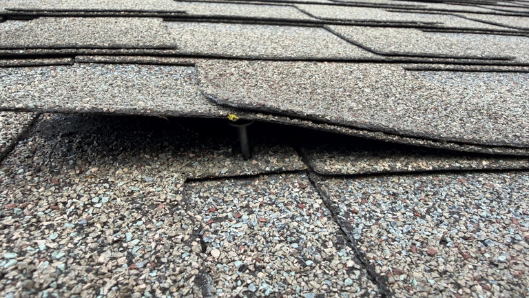 Close-up of a shingle edge showing a raised roofing nail